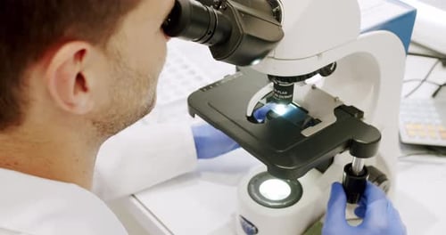 Man in Lab Coat and Latex Gloves Using Microscope to Examine Sample