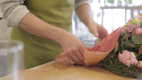 Young florist man expertly wrapping a beautiful flower bouquet at his shop