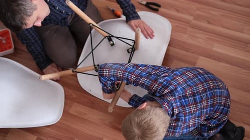 Father and Son Assemble Furniture From Small Parts Little Boy Helps His Father to Assemble a Chair