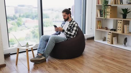 Man Relaxing on Beanbag Chair Using Smartphone