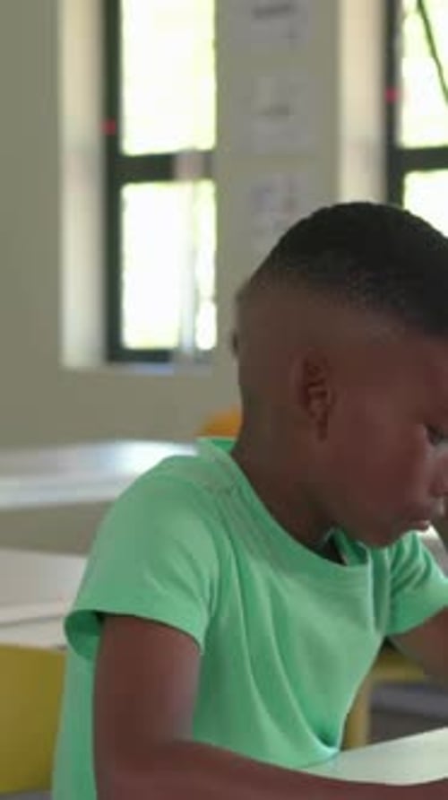 Vertical video: Leaning, boy in green T lifting phone showing, tapping and reading at desk in class