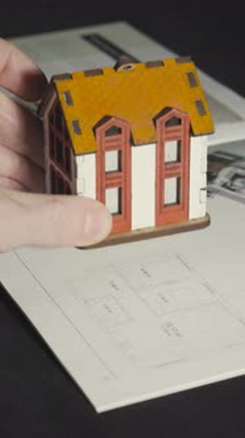 A Hand Places a Small House on an Advertisement Brochure