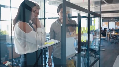 Young business people in formal clothes planning work in the office with paper stickers on the glass