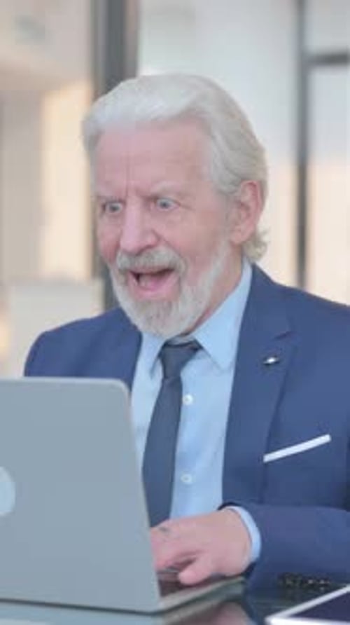 Senior Man Celebrates Success with Laptop Indoors