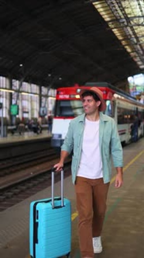 Smiling Young Man Walks with Suitcase in Train Station