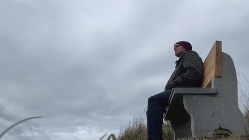 Man Looking Afar Sitting On The Bench Against Cloudy Sky. - low angle, static shot