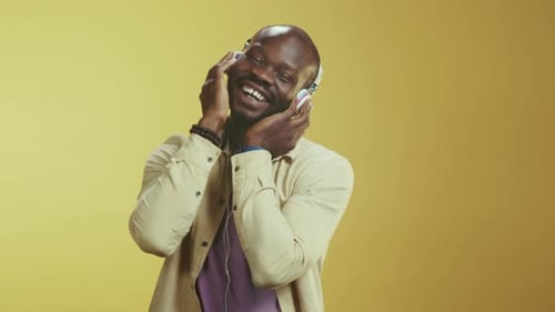 Man Enjoying Music with Headphones Against Yellow Background