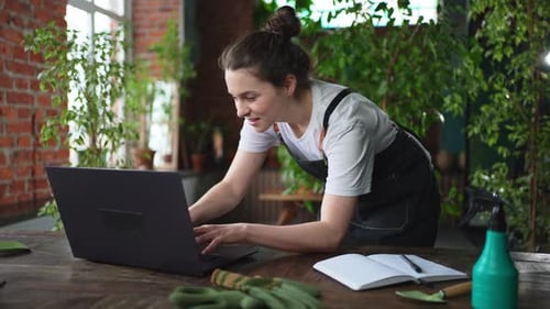 Female Florist Gardener Working in Botanical Store Greenhouse Using Laptop Order Plants