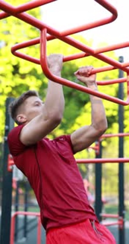 Athletic young man doing pull ups at outdoor gym, low angle view
