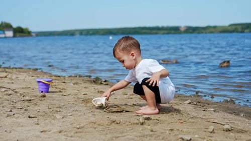 Little Caucasian boy in white t-shirt digging sand on the beach.