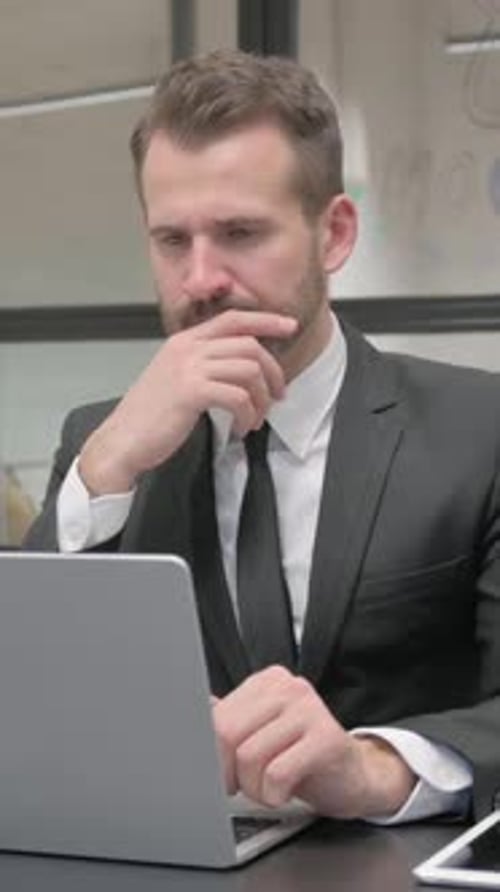 Thoughtful Businessman Working at Laptop in Office