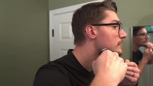 Man Trimming Beard with Electric Razor in Bathroom