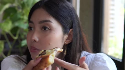 Beautiful woman wearing top white blouse eating pizza at a cafe for lunch.