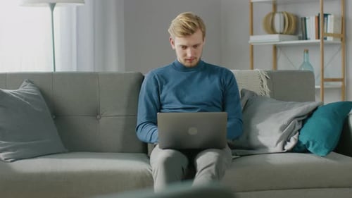 Young Man Works on Laptop on Sofa