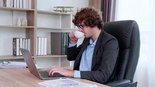 Young caucasian businessman using laptop computer planning for success and drinking coffee.