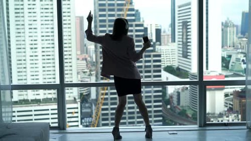 Attractive businesswoman dances to music by window with city view at home