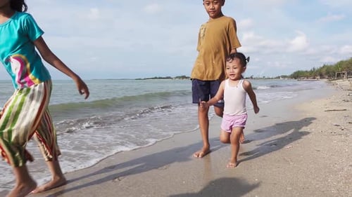 An adorable little girl running on the beach, chasing her brother in slow motion