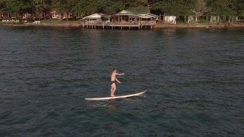 Aerial drone bird's eye view of man exercising on a sup paddle board in turquoise tropical clear wat