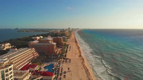 Tropical sea waves crashing on white sandy shore with a blue sky, golden sun rays shine on turquoise