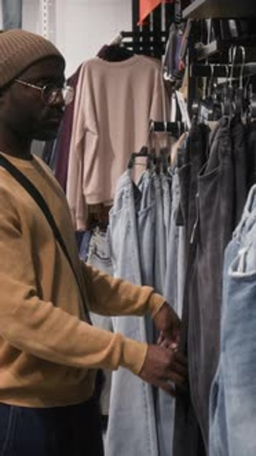 Vertical of Black Man Choosing Jeans in Clothing Store