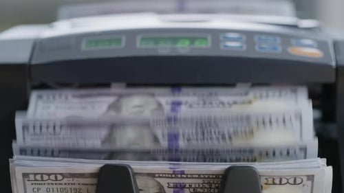 Closeup of a money counting machine tallying stacks of United States dollar bills