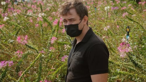 Young Male Caucasian Man with Face Mask Stands in Blooming Spring Flower Field
