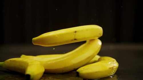 A Branch of Three Bananas Falls on the Table Forming a Spray of Water