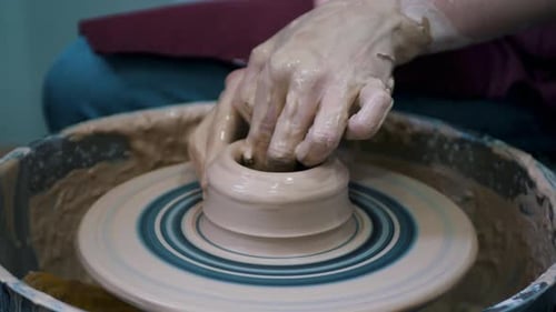 Close-up of potter's hands covered with clay making beautiful vase on throwing wheel in pottery work