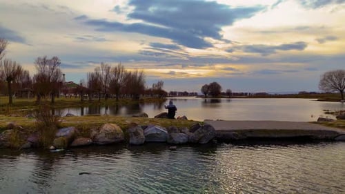 Man Fishing Alone By The Lake At Sunset