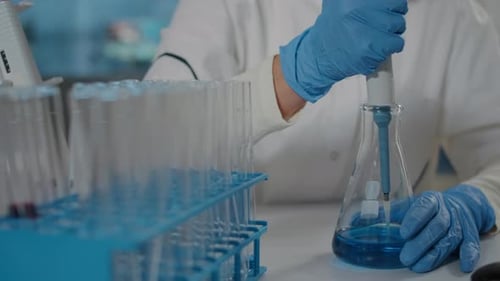 Scientist Using Pipette With Test Tubes and Flask