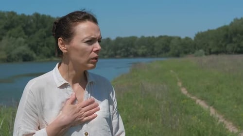Woman Using Inhaler by the River on Sunny Day