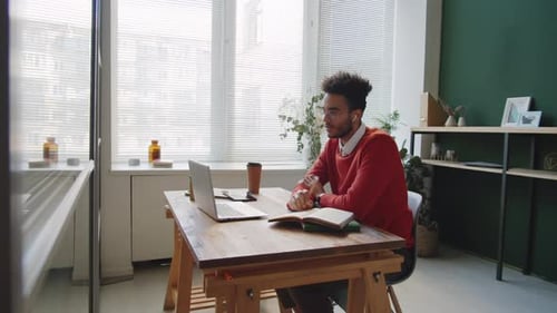 Young Mixed Race Man Talking on Web Call and Taking Notes in Office