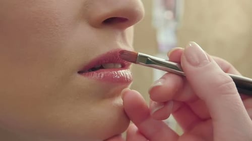 Maskenbildner verwendet Pinsel, um Lipgloss auf Modellippen aufzutragen