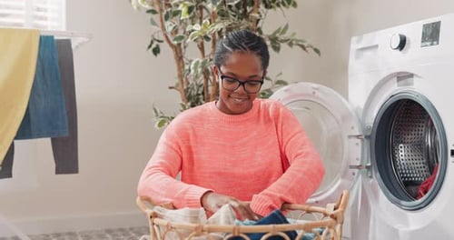 Woman in Glasses Performs Household Chores in Bathroom Laundry Room Kneels with Wicker Basket Filled