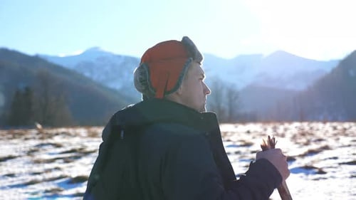 Young Hiker Goes Nordic Walking with Sticks on Snowy Field at Mountain Background. Sporty Guy