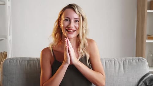 Blonde Woman Expressing Joy with Hand Gestures on Couch