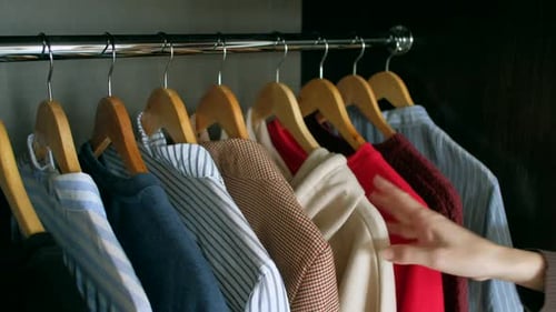 Hand Sorts Through Hanging Clothes in Wardrobe