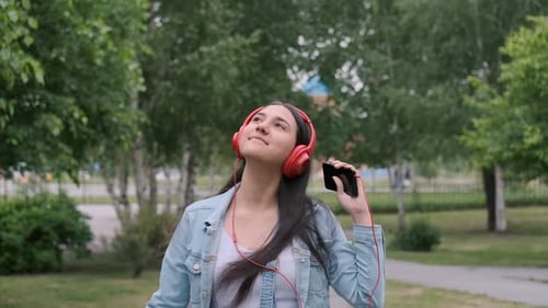Cheerful Girl in Headphones Walks on the Street