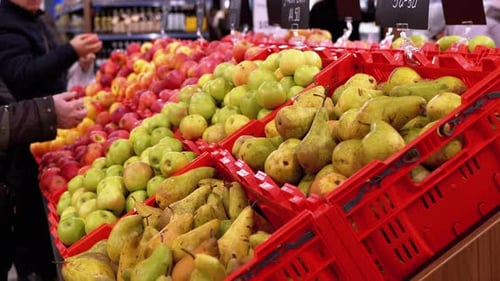 Früchte mit Preisschildern an einem Schaufenster in einem Supermarkt und vorbeigehende Käufer.