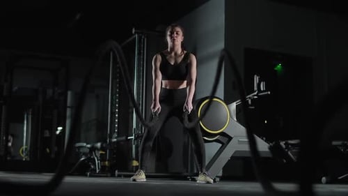Kaukasische athletische Kämpferin führt Übungen mit Battle Ropes Ausdauertraining in der