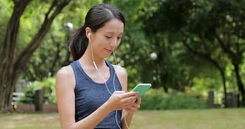 Sport Woman Listen to Music on Cellphone with Earphone in The Park