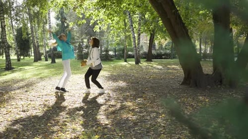 Two Caucasian Women Tossing Yellow Leaves in the Autumn Park. Joyful Family Spending Sunny Day
