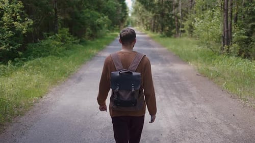 Ein Tourist mit einem Rucksack geht in einem Waldgebiet die Straße entlang und schaut sich um