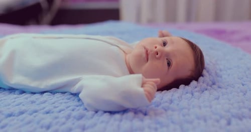 Pretty Little Baby Lies on the Bed and Looks Around, Smiles and Moves His Mouth. Portrait View.