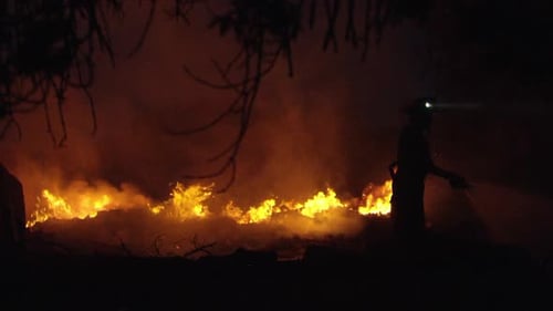 Fireman spraying water on fire after dark
