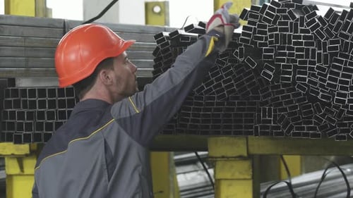 Rückfahraufnahme eines männlichen Lagerarbeiters, der Metallrohre im Regal organisiert