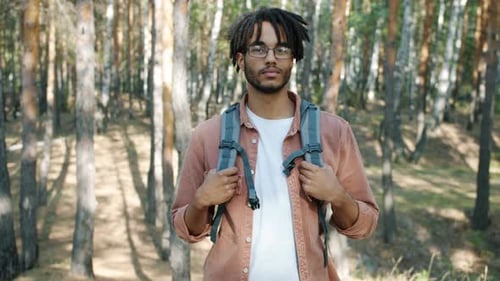 Porträt eines gut aussehenden afroamerikanischen Wanderers mit Rucksack, der an einem sonnigen Sommertag im Wald steht
