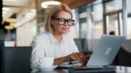 Lächelnde Geschäftsinhaberin arbeitet mit Laptop im gemütlichen Café und genießt Gerät