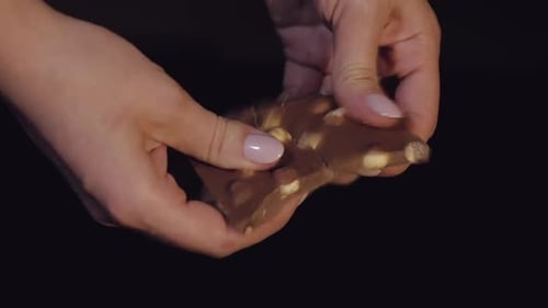 Woman Breaks Black Chocolate Bar with Nuts