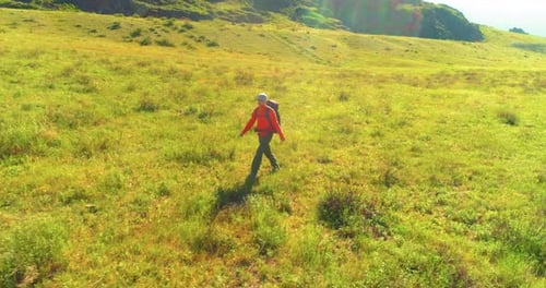 Flight Over Backpack Hiking Tourist Walking Across Green Mountain Field, Huge Rural Valley at Summer